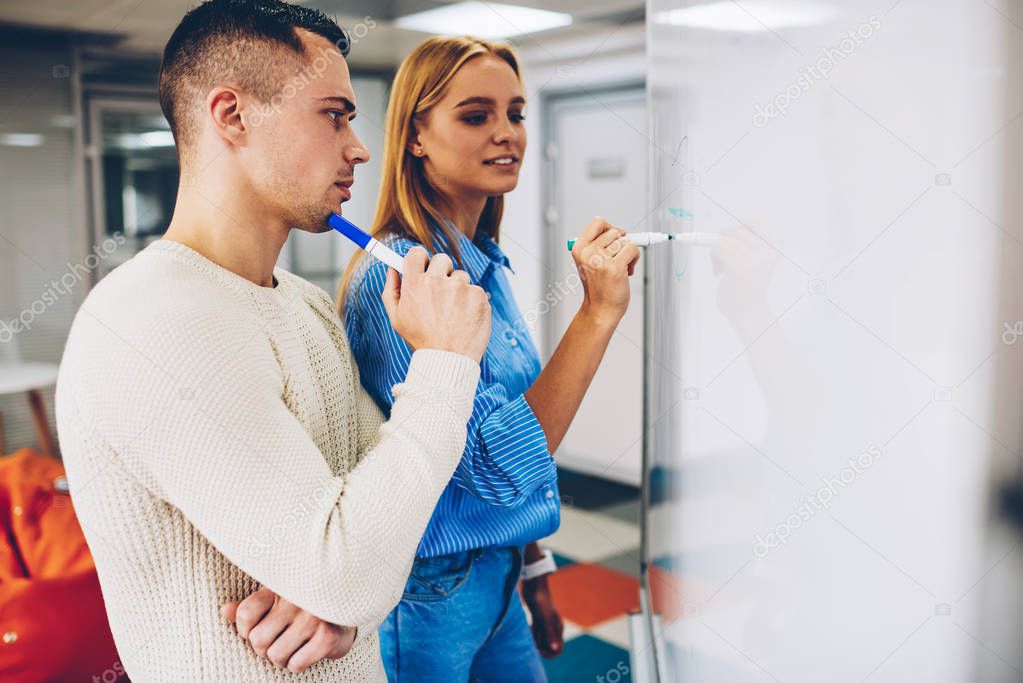 Young skilled employees solving project standing near board to writing creative ideas for discussing,male and female colleagues planning startup strategy talking about business noting points