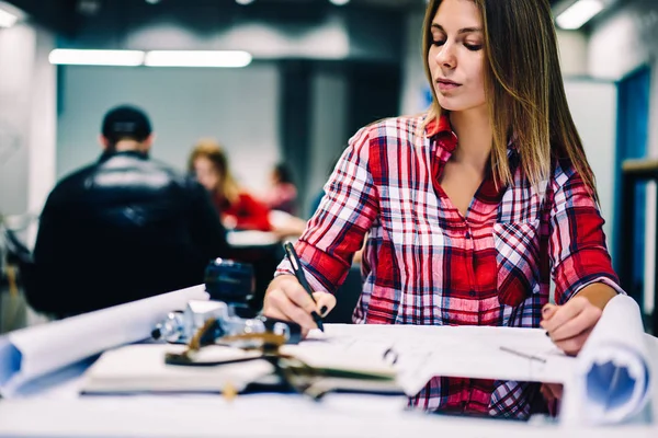 Concentrated female student drafting blueprint for coursework sitting at college library, talented woman designer drawing sketch on paper for project thinking about accountings and ideas during working