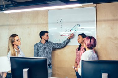 Flip grafik üzerinde şık sınıfta okuyan gereç açıklayan diyagramı ile işaret eden koç genç adam. Grup başarılı öğrenci ders sırasında gemide teamworking çizilmiş grafik tartışıyor