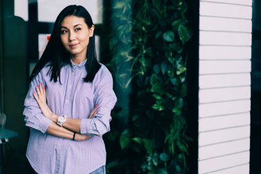 Çekici olumlu yetenekli kadın işçiye serin gömlek ayakta fikirleri hakkında düşünürken cam duvara. Genç güzel mutlu esmer kadın modern ofiste vakit süre durulması