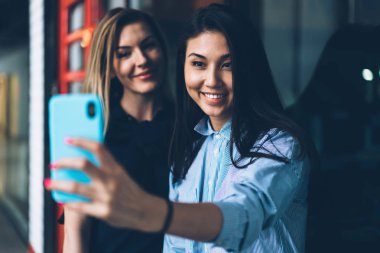 Birlikte ağ profil resmi güncelleştirmek için smartphone kamera çekim müreffeh hipster kızlar çekici genç. Sevimli gülümseyen kadın boş vaktinizi ofiste iş molası sırasında