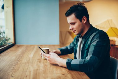 Yeni arkadaş ekleme ve takipçileri ile genç erkek sabah haber web sitesi üzerinden cep wifi kafede kullanarak okuma sohbet ara smartphone üzerinden ağ dalgın teen hipster adam