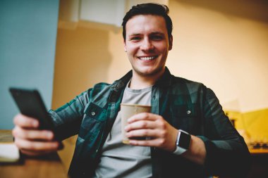 Neşeli genç adam ağ telefon, müreffeh erkek blogger takipçileri smartphone üzerinden sohbet için iyi Wi-Fi bağlantısı ile kafeteryada oturan eğlence üzerinde favori kahve zevk