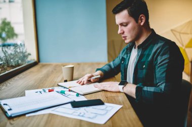 Genç adam akıllı erkek öğrenci ile kağıt ve Kırtasiye kafede oturan üniversite sınavları için hazırlık kurs projesinin planlama iç yapım coworking uzayda öğrenme konsantre