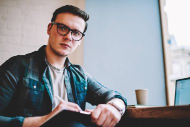 Gözlük vizyon düzeltme mesafe iş sürecinde, profesyonel erkek serbest kamera Cafe bakarak yayın makaleleri notlar yapmak için ciddi hipster adam portresi