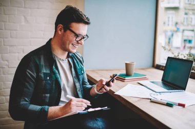 Komik video gülen neşeli genç adam Smartphone'da uzaktan kafede, çalışırken göz hipster adam üstünde email tebliğ üstünde telefon kontrol iyi haber alma ile memnun gülümsüyor