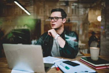 E ders, proje uzağa bakmak için bilgi analiz kafede dizüstü bilgisayar üzerinden uzak iş yapan düşünceli erkek öğrenme sırasında koruma vizyon durulması için Eyewear ciddi erkek öğrenci