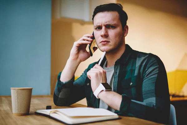 Portrait of upset young male disappointed with bad news during telephone conversation, young hipster guy calling to banking service operator having problems with ballance looking at camera worried