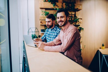 Dizüstü bilgisayar, internet bağlantısı üzerinde serbest togethe kazanç müreffeh Genç Girişimciler kullanan meslektaşı ile uzay coworking okuyan kamera bakarak neşeli hipster adam portresi