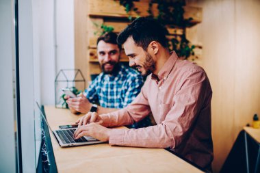 Yetenekli erkek bu geliştirici konsantre mesafe iş alanı, coworking içinde ödev bilgilerini Netbook camu içinde arama hipster adam gülümseyen meslektaşı ile oturan dizüstü bilgisayar üzerinden