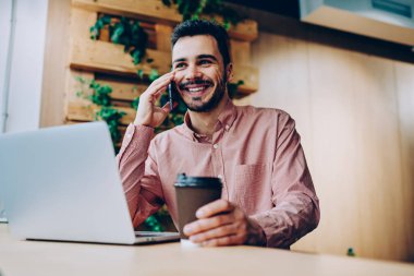 Uzaktan ofis, hipster adam zevk cep telefonu konuşma kahve Brea'daki gülümseyen yakışıklı coworking içinde dizüstü bilgisayar üzerinde çalışırken telefon görüşmesi müreffeh genç erkek serbest meslek