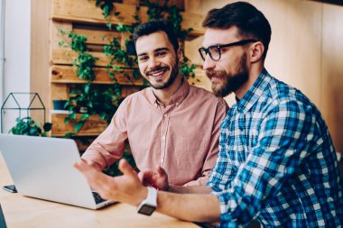 Kamera işbirliği yaparken, birlikte dizüstü bilgisayar kullanan projede çalışan yetenekli erkek programcılar açıklayan bilgi ve fikir onun arkadaşı süre bakarak neşeli yakışıklı adam portresi 