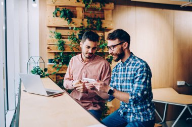 Hipster çocuklar birlikte ücretsiz vakit gülümseyen dijital tablet ve modern apps kullanarak online oyun oynamak ve campu boş zamanlarında konuşurken arkadaşına gösteren erkek holding touchpad sakallı