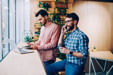 Genç gülümseyen hipster adam telefon görüşmesi sırasında meslektaşı erkek öğrencilerin kahve molası Gadget'ı kullanarak gerçek iletişim görmezden diz üstü bilgisayar ağlarında bilgi arama