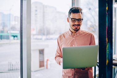 Genç hipster adam gözlük vizyon koruma dizüstü bilgisayar, netbook çalışma için iyi geri bildirimler hakkında mutlu neşeli erkek freelancer Gözat web sayfasında bilgi okumak için memnun