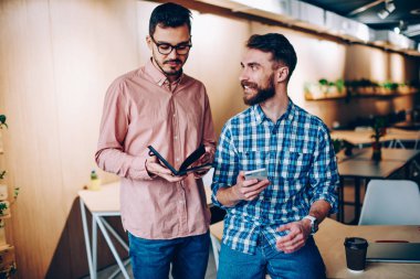 Neşeli hipster adam meslektaşı gülümseyen iletişim iş smartphone, bilgi iş arkadaşınız ile işbirliği için tartışmaya ile adam holding Not defteri kullanarak planlama hakkında ofiste bakarak