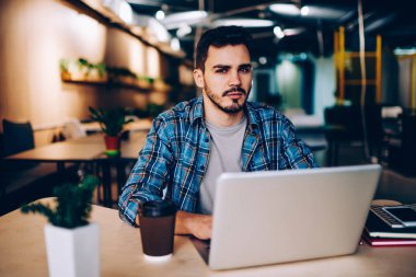 Üniversitede, Genç adam kamera sorun girintili coworking içinde dizüstü bilgisayar kullanarak hayal kırıklığına bakarak netbook ve wifi kullanarak sınava hazırlık için araştırma yapmak ciddi hipster adam portresi