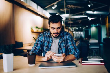 Bildirim gelir çıkıyor öğrenme için üniversite kafeteryada otururken hücresel, genç erkek yükleme uygulaması üzerinde cep telefonu sosyal ağlardan kontrol dalgın hipster adam