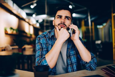 Düşünme düşünce hipster adam aver konuşurken telefonla arkadaşıyla kafede, müşteri destek hattı telefon fon üzerinde ile bağlantı bekliyor dalgın genç adam toplantı için planları