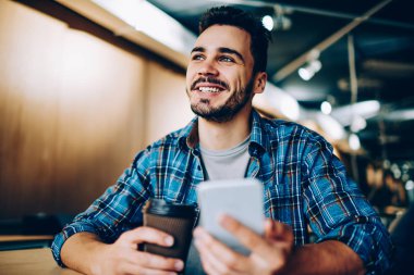 Neşeli yakışıklı adam bakarken hayal tatilini ofis, smartphone ile kahve molası cep telefonu ağ için elinde bir şey hakkında hayal öğrenci gülümseyen genç sohbet ederken