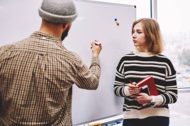 Hipster öğrenci yazma örnekleri ile profesyonel erkek eğitim ders sırasında gemide ödev öğretmek. Genç adam düzeni şık coworking uzman ile atölye çalışması sırasında flipchart üzerinde çizim