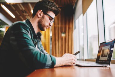 Telefon app denetleme çalışma işlemini Planlama şık kıyafeti giymiş yakışıklı yaratıcı erkek tasarımcısının resim kırpılmış. Sakallı ciddi adam cep üzerinde yararlı bir araç kullanarak müşteri ile sohbet