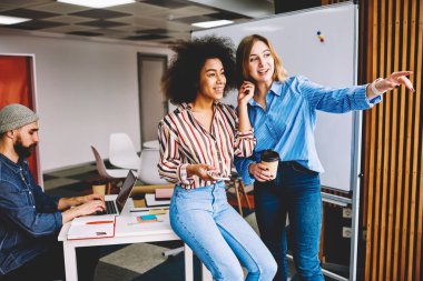 Eğleniyor birlikte modern ofiste işbirliği ise genç akıllı iyi görünümlü kadın iş arkadaşları. Başarılı hipster kızlar erkek partner dizüstü bilgisayarda çalışma sırasında kapalı gülüyor