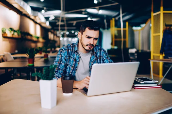 Yorgun genç erkek öğrenci üniversite sınavlarına hazırlanıyor dizüstü bilgisayar netbook düşünme overworked üzgün freelancer okuma bilgileri problem çözümü hakkında sıkıcı webinar izlerken 