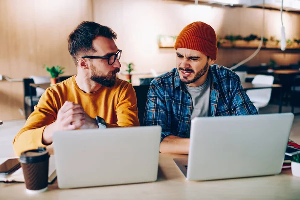 Annoyed hipster guy communicating with colleague about  problem with cooperation sitting with laptop together, angry young man talking with friend about bad news about college feeling irritatio