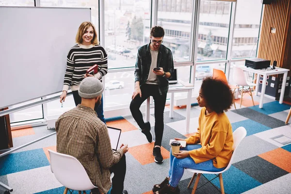 Portrait of successful female coach conducting training design session for creative multicultural students in stylish coworking space.Diversity group of young designers teamworking on common project