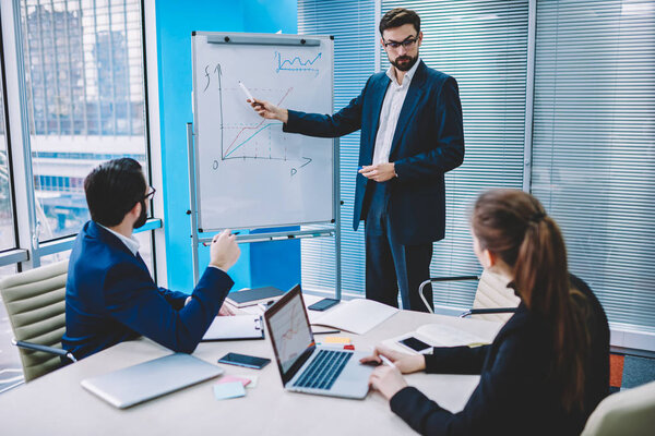 Группа офисных перспективных работников на деловой встрече, профессиональные партнеры, присутствующие на презентации о будущем компании, менеджер показывает график и цифры плана для эффективных результатов
