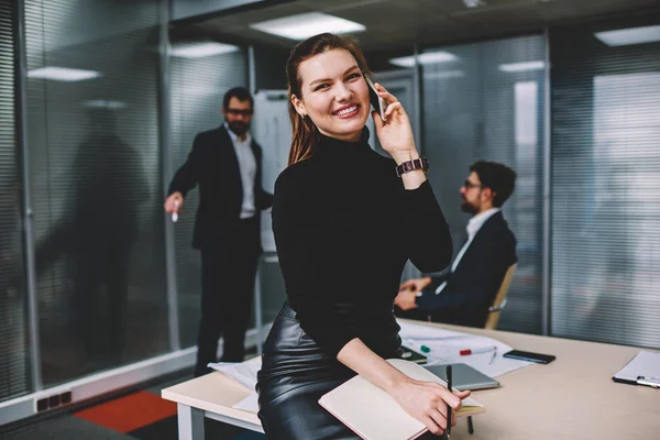 Portrait of cute young female secretary talking on cellular with colleagues on background,  attractive successful businesswoman calling using new modern smartphone, girl smiling and looking at camera