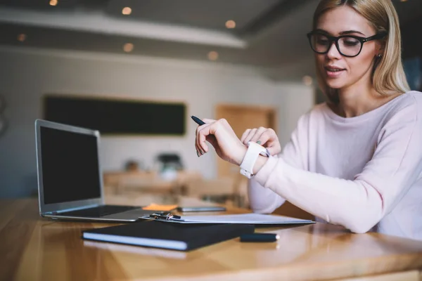 Mulher Bonita Olhando Smartwatch Sentado Mesa Com Computador Portátil Moderno — Fotografia de Stock