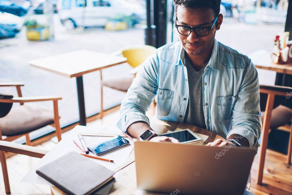 Cropped image of talented professional designer in eyeglasses sending email message in website on laptop computer connected to wifi.Smart male architect chatting with customer while sitting indoors