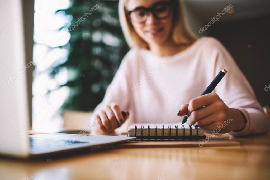 Young women writer scribing notes to her notebook for future romance, girl trying to note new ideas near desktop with modern laptop computer, female writing plan for tomorrow creating to do list