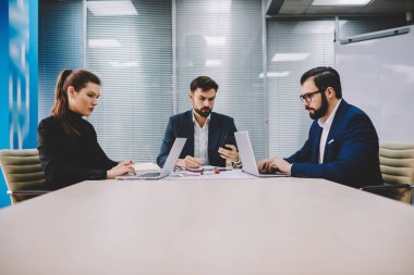 Dalgın iki profesyonel finans şirketi patronla tablo toplantıda çalışma brifing sırasında dizüstü bilgisayarlarda bilgi aramak. Gurur CEO'su posta smartphone meslektaşları ile işbirliği üzerinde kontrol