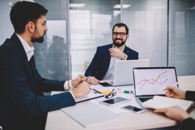 Formal Giyim tablo office iç netbook'lar ile Toplantı oturan iş meslektaşları ile tartışma sırasında ortaklık ayrıntılarını gülüyor pozitif profesyonel erkek girişimci giymiş