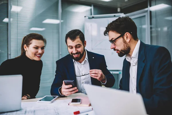 Genç yetenekli gülümseyen iş arkadaşlarınızla birlikte smartphone cep telefonu ile Web sitesi komik video izlerken iyi internet'e bağlı. Grup çalışma molası sırasında eğlenmek akıllı duygusal Mimarlar