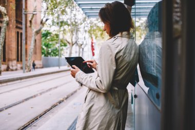 Şık genç kadın modern Dokunmatik ped aygıt yolu ile 4 g internet ayakta tramvay durağı kentsel ortamda online ödeme yapma ceket giymiş. Hippi kız online dijital tablet Caddesi üzerinde chattin
