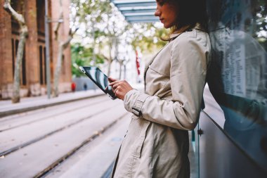Posta kontrol ve bildirim istimal özgür 4 g dokunmatik yüzey üzerinde okuma trendy ceket genç kadın yan görünüm kırpılmış Internet. Dalgın kadın blogger profil sayfası tramvay durağı tablet ayakta güncelleştiriliyor