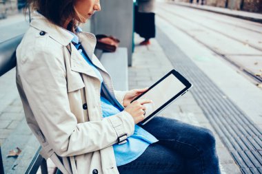 Tramvay durağı üzerinde oturan 4 g internet bağlantısı ile modern tablet medya dosyalarını seçerek şık genç kadın yan görünüm kırpılmış. Beyaz kadın dijital dokunmatik yüzey boş ekranda metin yazma