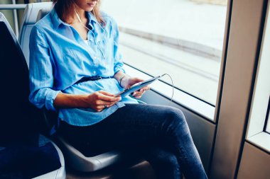 Tramvayda oturan halk için ücretsiz wifi taşımak için izlerken eğitsel online modern Dokunmatik ped cihaz bağlı kulaklık hipster blogger görünümünü kırpılmış. Genç kadın tablet müzik dinleme