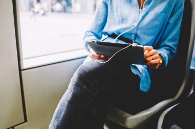 Dokunmatik yüzey üzerinde sosyal ağlar sohbet ve kulaklık bağlı tramvayda oturan aygıt radyo dinleme kadın yolcu görünümünü kırpılmış. 4 g kullanarak dijital tablet holding kadının eller Internet