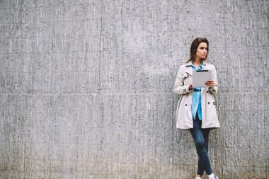 Düşünceli beyaz genç kadın giyinmiş rahat kat uzakta 4 g ile modern dokunmatik yüzey üzerinde app yüklerken bakarak Internet. Kadın blogger ile tablet ayakta promosyon arka plan üzerinde durulması