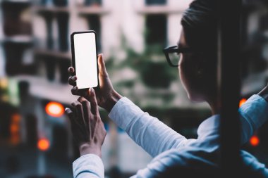 Omuz kadın kişinin parmak kopyalama alanı ekranı modern smartphone bokeh ışıklar arka plan açık havada duran ile dokunmadan görünümünden arka. Cep telefonu uygulamaları ile internet kullanan kadın