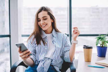 Yeni veri kaynağı ve sosyal ağlar üzerinden smartphone içeriğinde ofis, takipçileri iletileri deskto oturma sevimli kadın blogger memnun mutlu kahve molası sırasında denetleme neşeli genç kadın