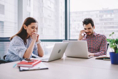 Konsantre erkek ve kadın çalışanların ofis, okul sırası vasıl kadın meslektaşı ile oturma çalışma işlemi sırasında cep telefonu üzerinde konuşurken adam araştırma yapmak için dizüstü bilgisayarlar kullanarak haber bağlantılı okuyun