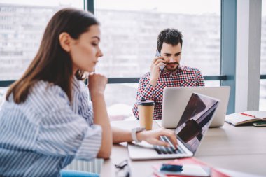 Erkek çalışan cep telefonu ofis, dizüstü compute kullanarak iş için online araştırma yapmaya konsantre kadın çalışma işlemi sırasında ağ dizüstü bilgisayarı üzerinde rezervasyon yapmak konuşurken tarih seçici odak