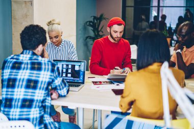 Smart casual giyinen yaratıcı gençlerin çeşitli takım giymek şık ofis kablosuz internet'e bağlı dizüstü bilgisayar ile masada oturan işbirliği sürecinin tartışırken planı