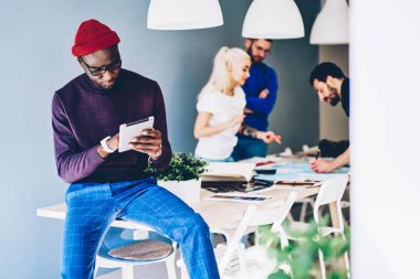 Afrikalı-Amerikalı genç adam 4 g kullanarak dijital tablet uygulaması güncelleştiriliyor konsantre internet meslektaşları teamworking arka planda office üzerinde iken. Dokunmatik yüzey üzerinde ödeme yapmadan dalgın hipster adam